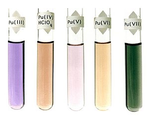 五支盛装着溶液试管：蓝紫色、贴有标签“Pu(III)”；深棕色、贴有标签“Pu(IV)HClO4”；浅紫色、贴有标签“Pu(V)”；浅棕色、贴有标签“Pu(VI)”；墨绿色、贴有标签“Pu(VII)”。